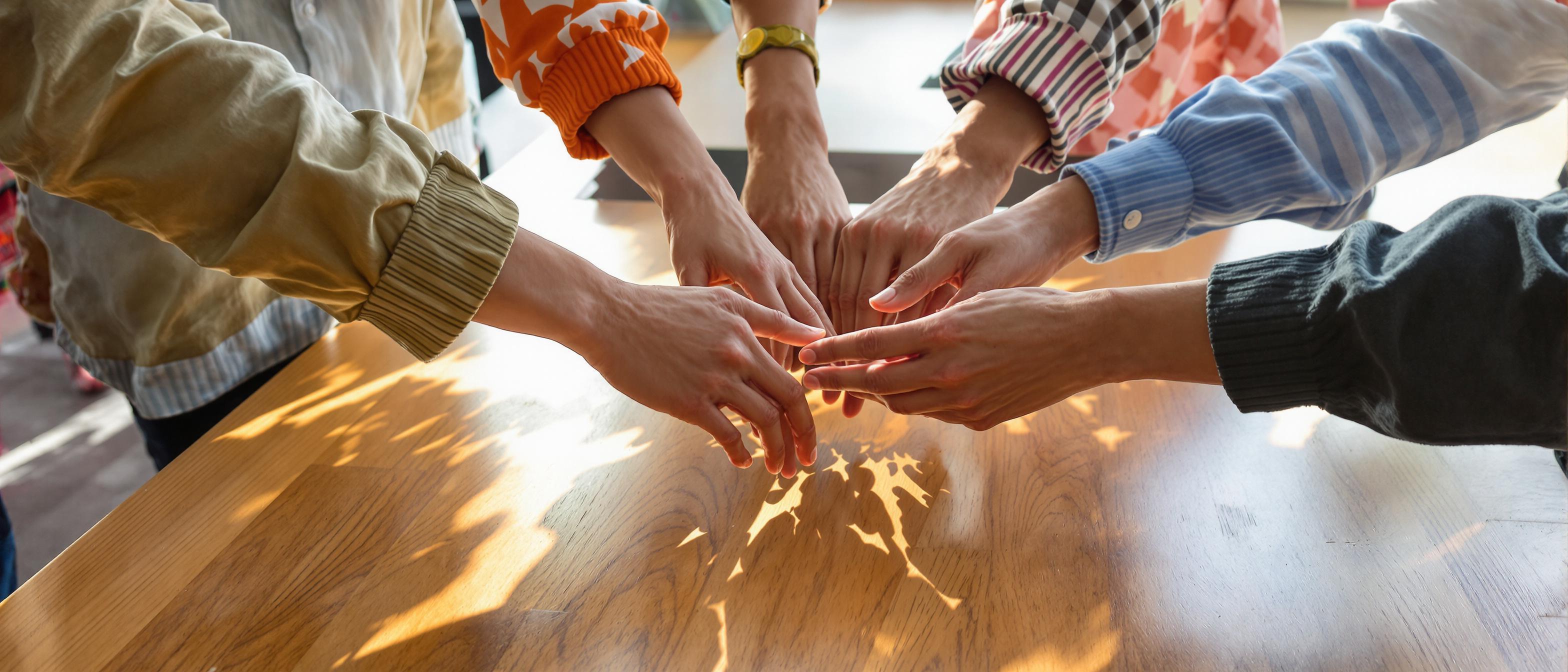A collaborative workspace featuring hands reaching toward a blank paper, bathed in natural light.