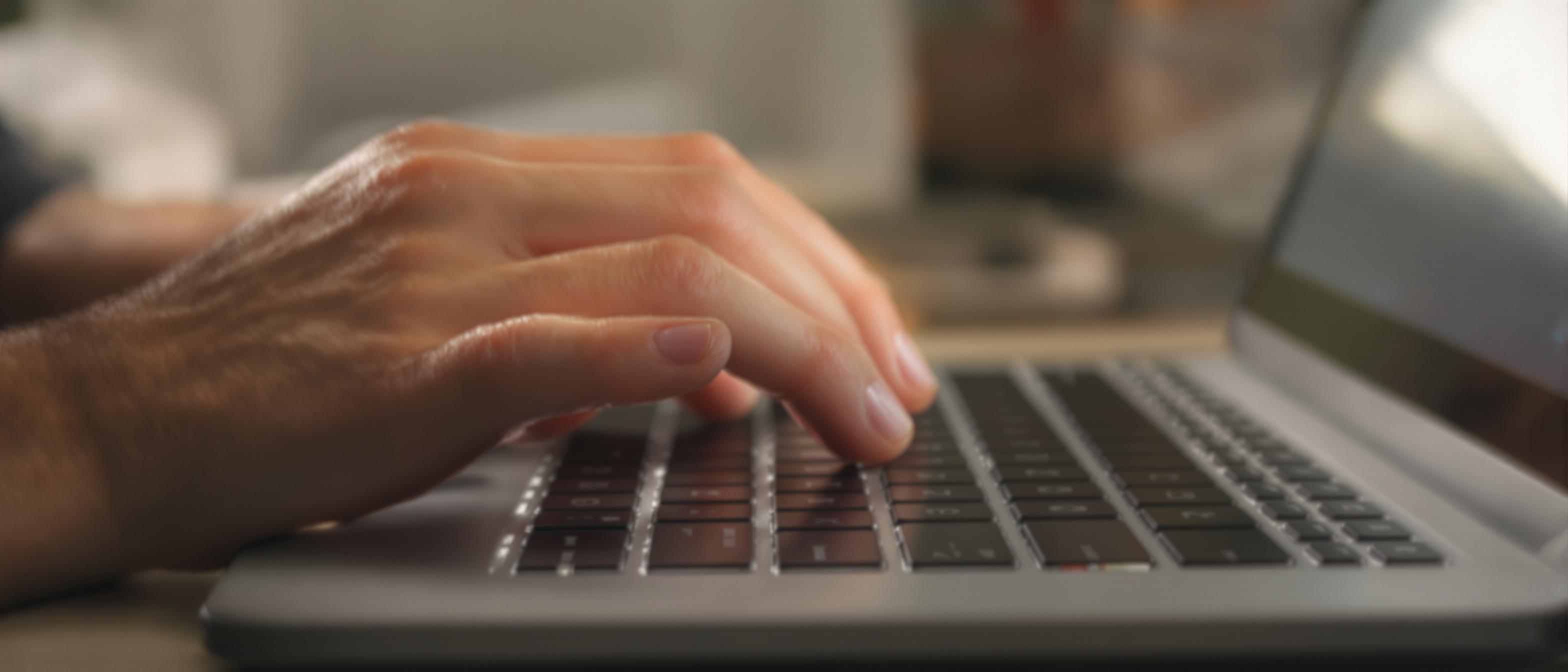 A person's hand reaches towards a laptop keyboard in a softly lit environment.