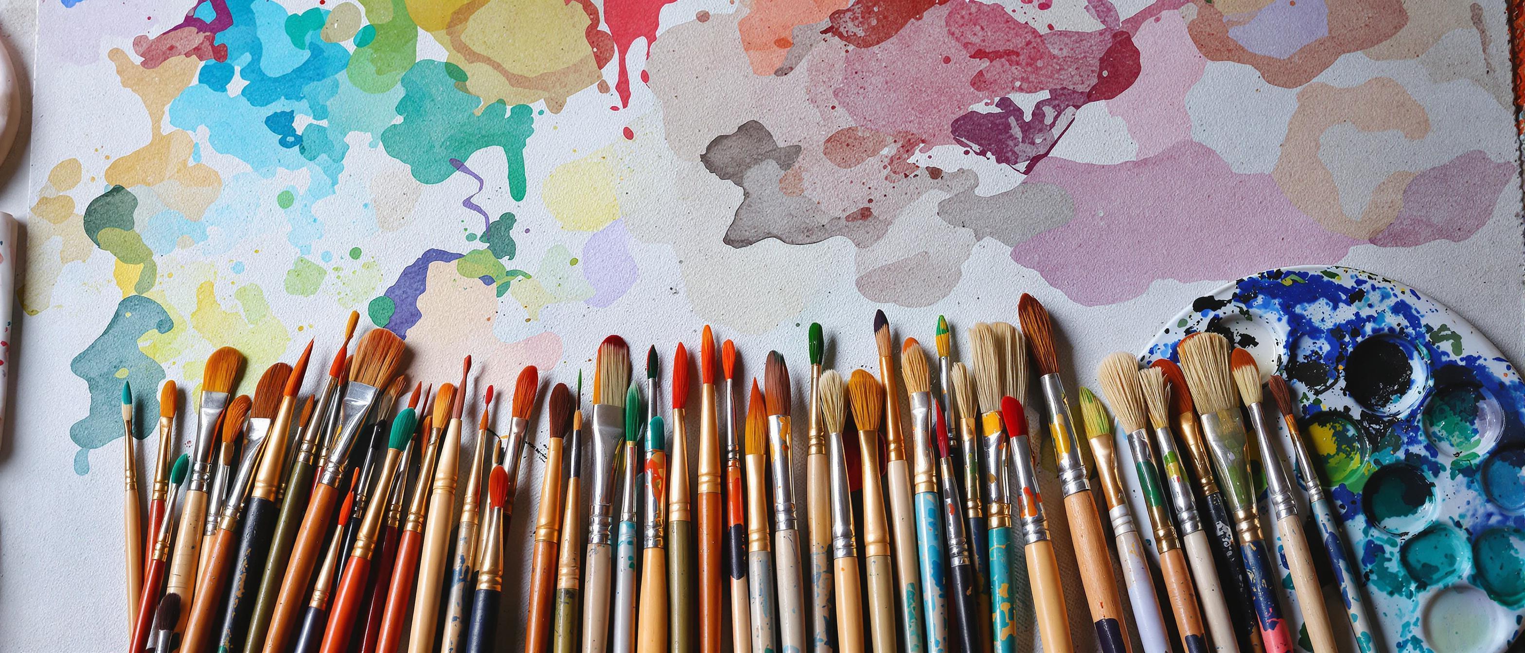 A vibrant arrangement of paintbrushes and watercolor palettes on a textured canvas, bathed in soft, diffused studio light.