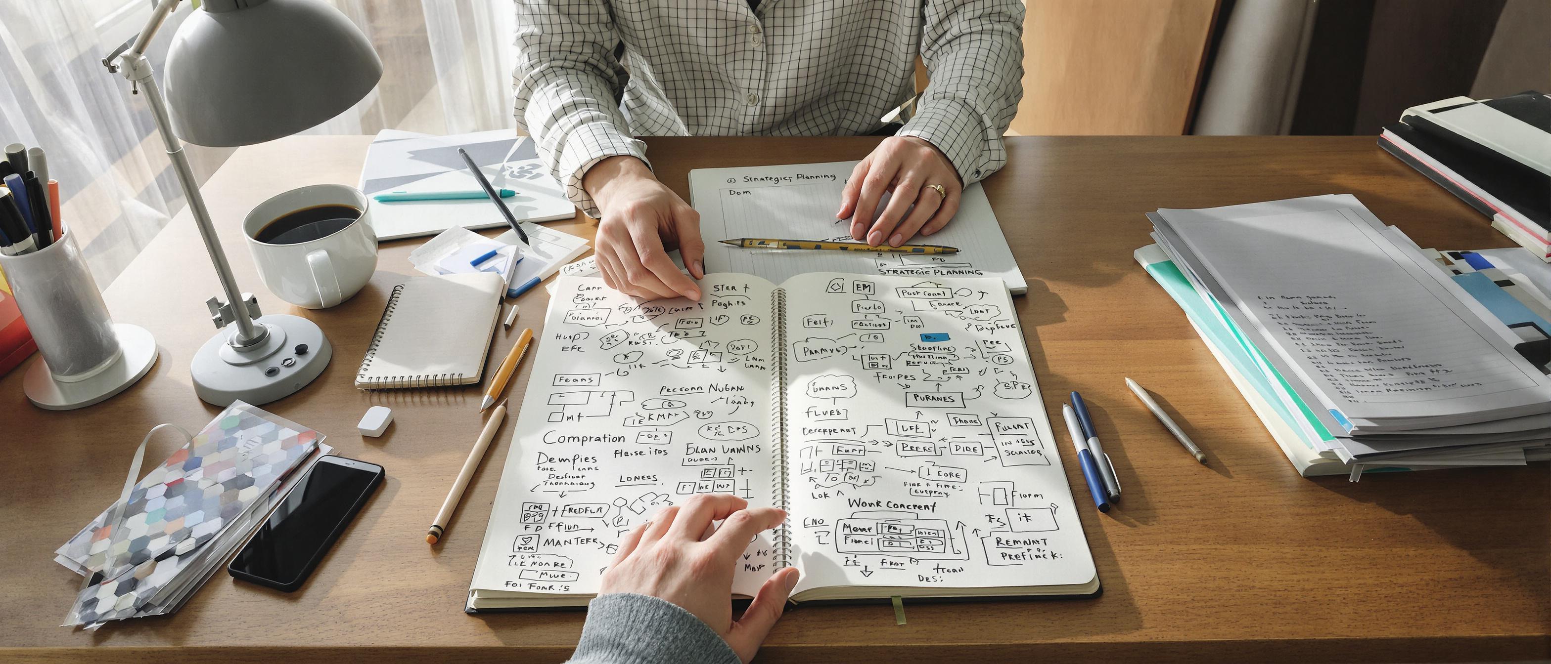 A person works at a desk with a laptop and notebook, surrounded by brainstorming sketches in a creative and organized setting.
