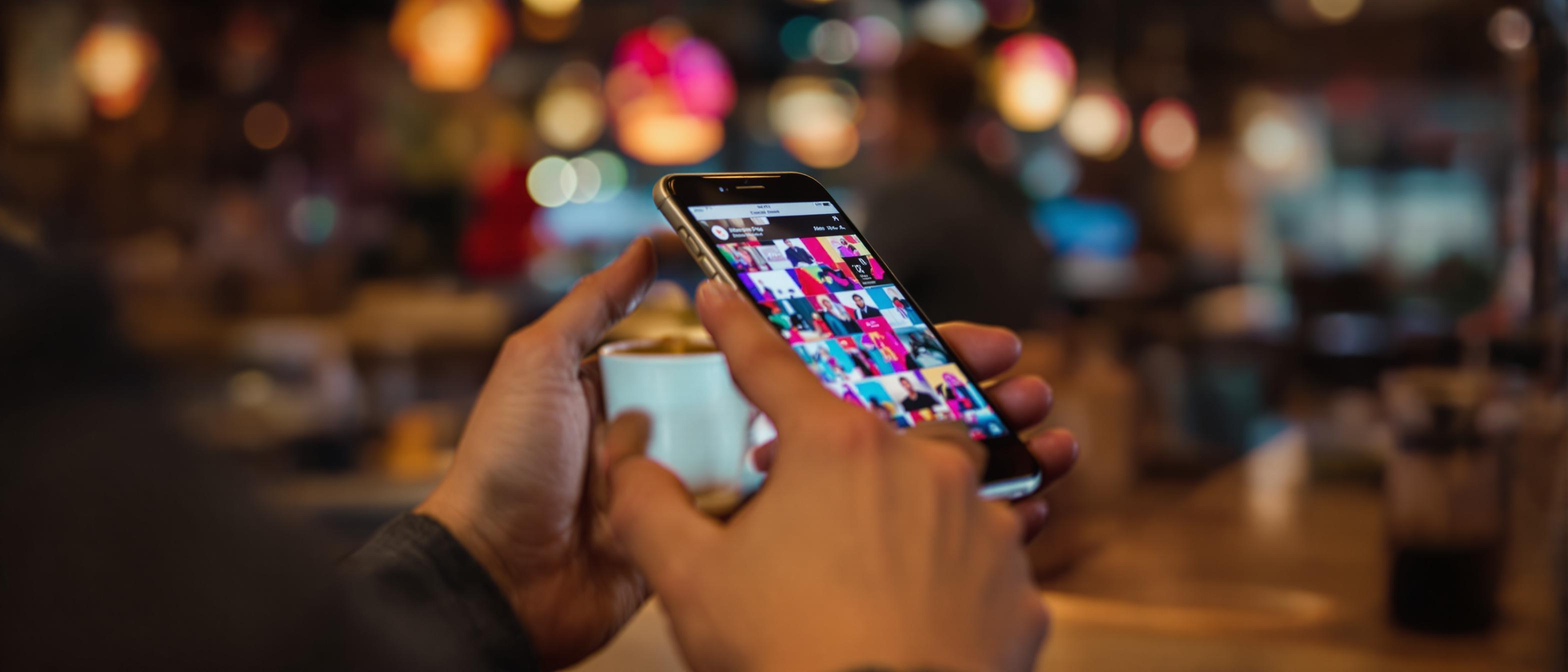 A person's hands holding a smartphone with a blurred background suggests being engrossed in digital engagement.