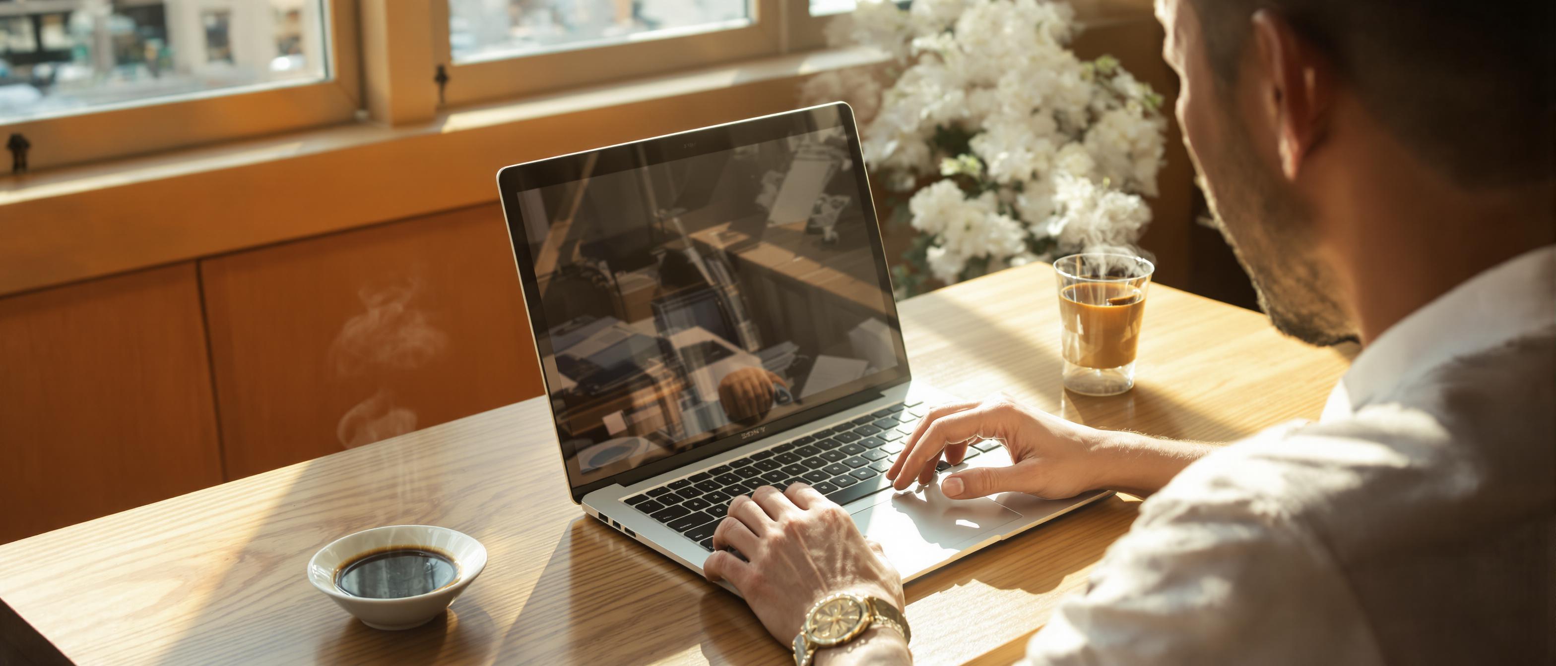 A person is using a laptop in a brightly lit cafe, focusing on the screen as if researching something important.
