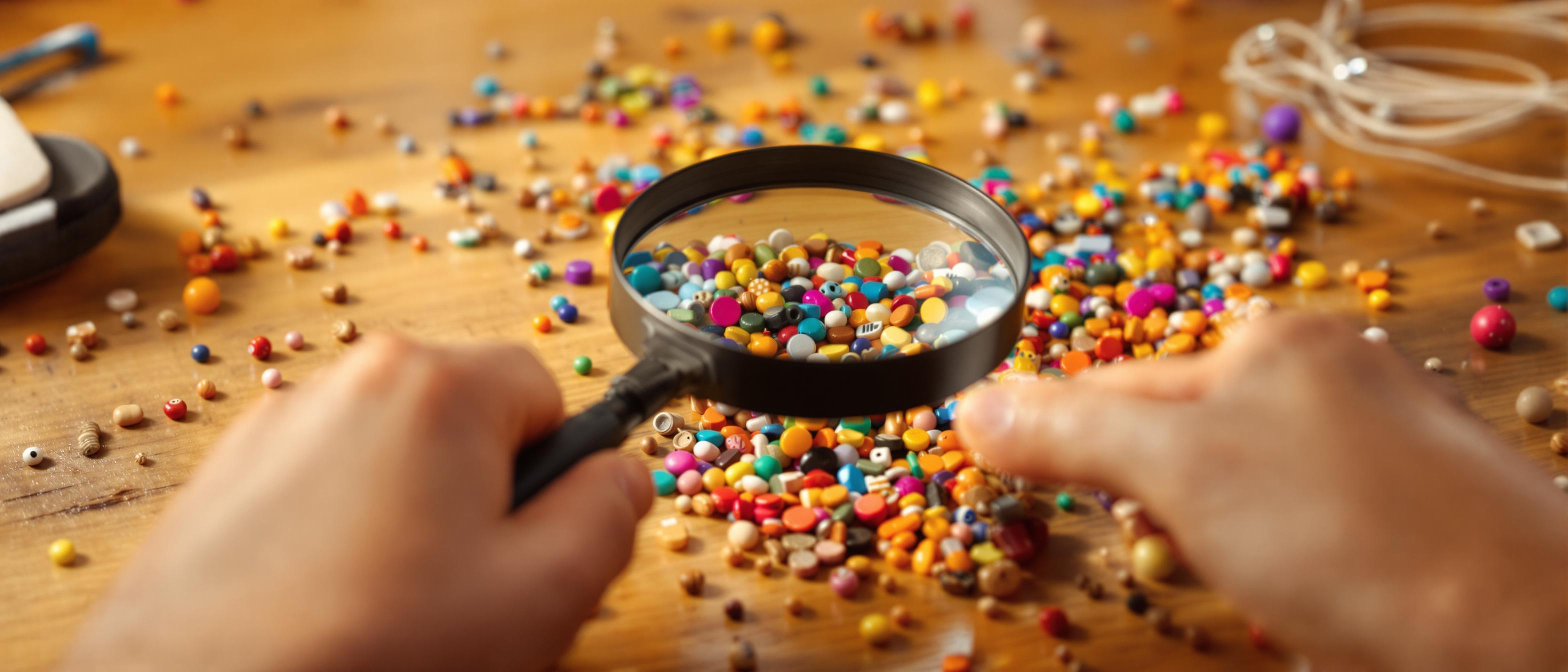 A person closely examines a colorful arrangement of objects on a table, using a magnifying glass to highlight details.