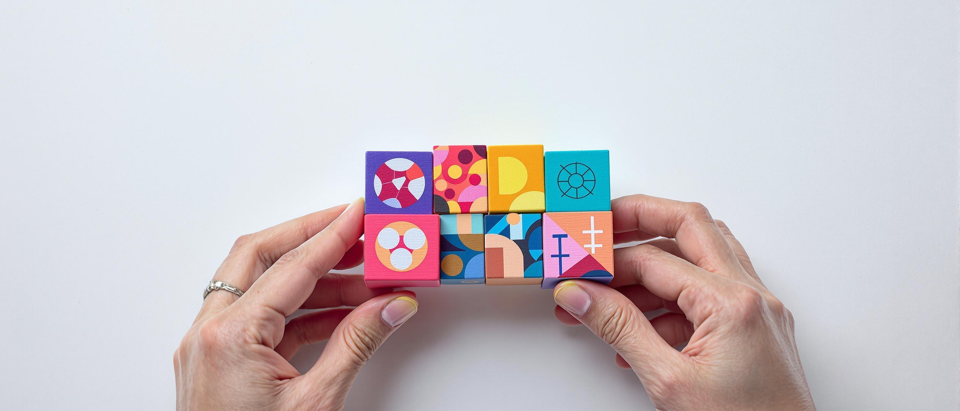 A person's hands carefully arranging colorful building blocks with abstract symbols, representing the construction of a brand identity.