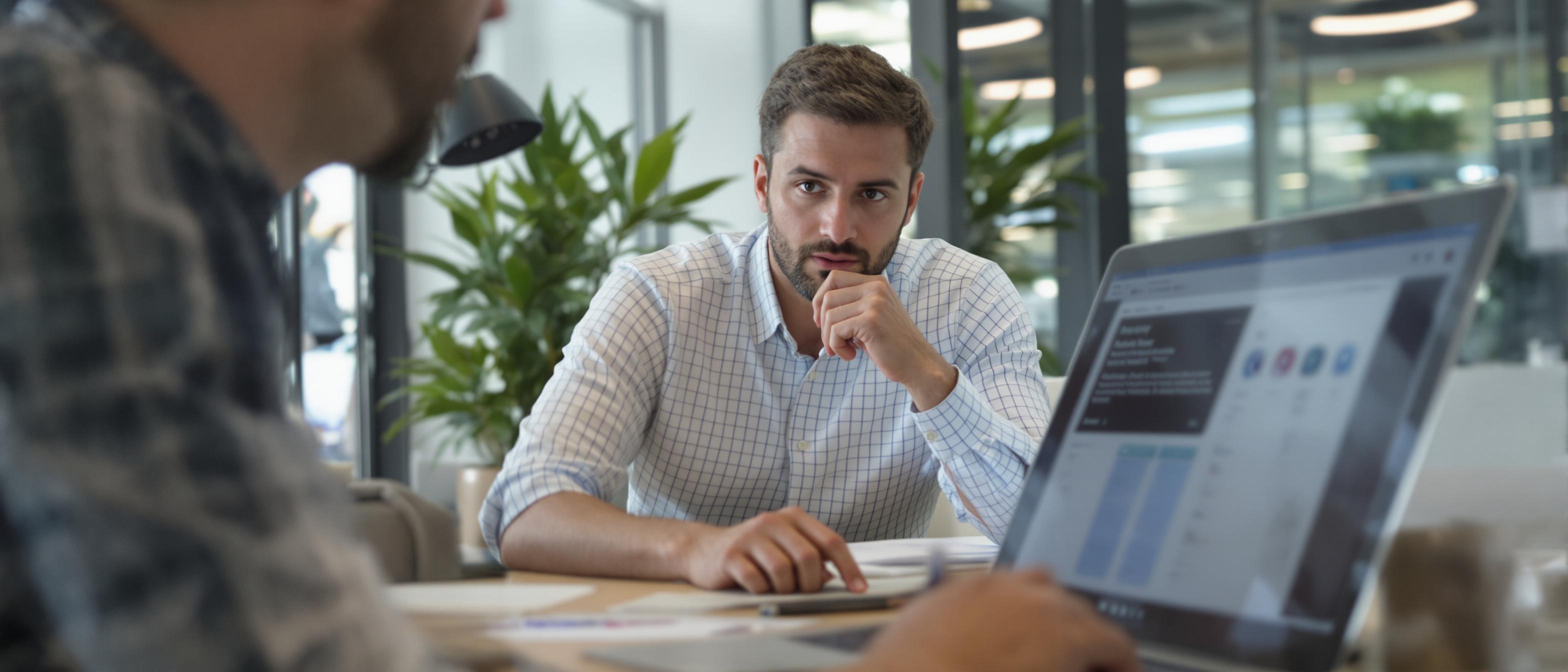 A researcher attentively observes a user interacting with a website on a laptop in a well-lit office environment.
