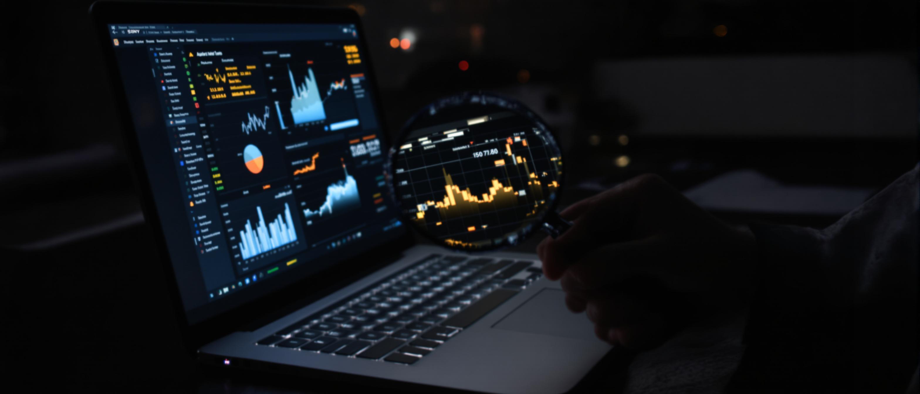 A hand with a magnifying glass examines a laptop screen displaying data analytics.